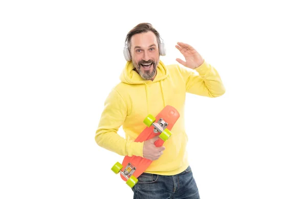 Šťastný muž skateboardista poslouchat hudbu ve sluchátkách držet skateboard izolované na bílém, baví. — Stock fotografie