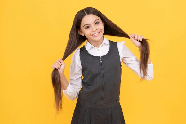 Happy teenage girl in school uniform smile holding long hairstyle yellow background, hair — Stock Photo, Image