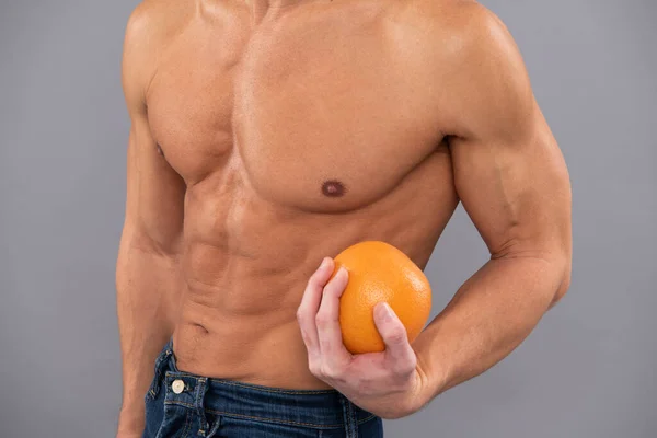 Ajuste a vista cortada do homem com seis abs do bloco torso muscular prendem a fruta alaranjada como símbolo da dieta, vitamina c — Fotografia de Stock