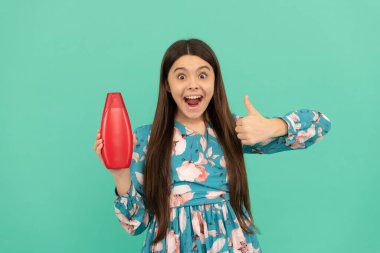 Şaşırmış uzun saçlı çocuk şampuan şişesini tut baş parmağını kaldır, cilt bakımı