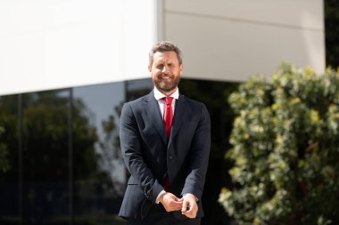 Takım elbiseli ve açık havada kırmızı kravatlı neşeli yakışıklı iş adamı.