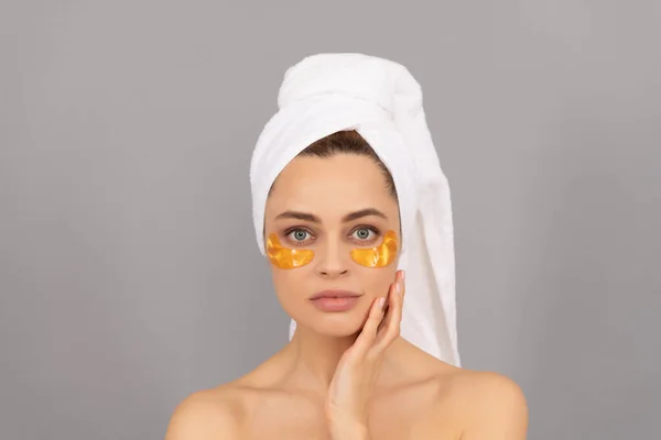 Ung kvinna med frotté handduk använda ansiktsbehandling gyllene ögonlapp för hud, hudvård — Stockfoto