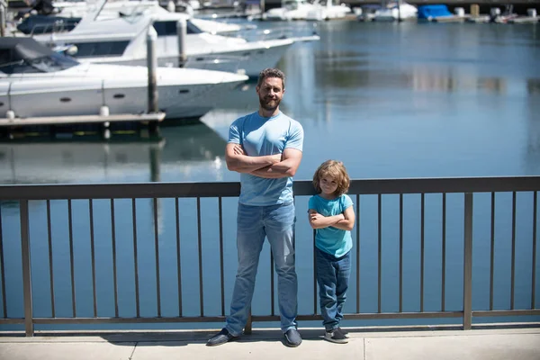 Happy father man and son child stand on quay railing keeping arms crossed with confidence, fathers day