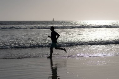 Spor adamı silueti yaz plajında deniz suyu ve güneşle koşuyor.