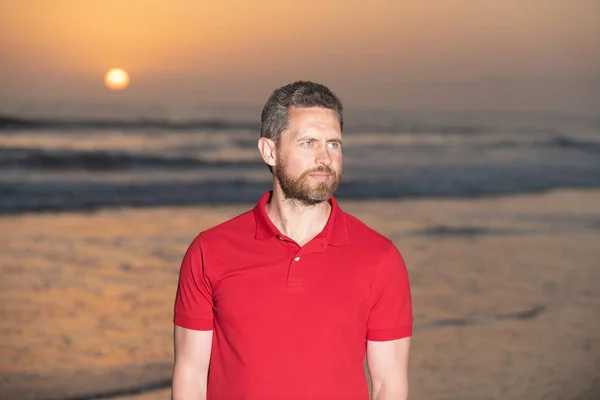 Barbudo bonito homem no verão camisa na praia com pôr do sol sobre o mar, relaxar — Fotografia de Stock