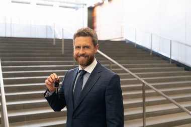 Gayrimenkul. Takım elbiseli mutlu adam arabanın anahtarlarını tutuyor. Olgun başarılı iş adamı ev anahtarıyla