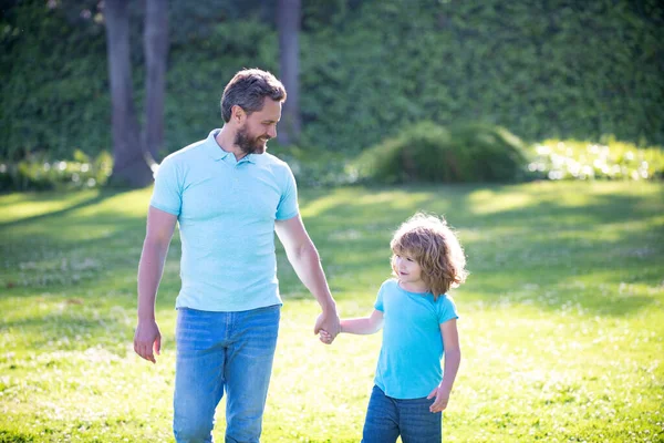 Feliz hijo y padre tomados de la mano caminando en el soleado día de verano en la hierba del parque, la paternidad — Foto de Stock