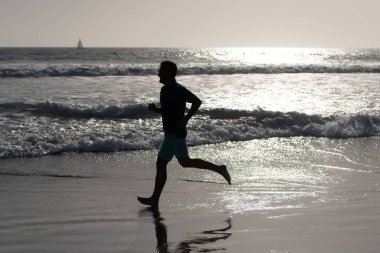 Sporcu okyanusta kazanmak için hızlı koşar. Sabah sporu aktivitesi. Sahilde koşan sağlıklı bir adam..