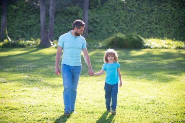 Mutlu oğul ve baba, güneşli bir yaz gününde parkta, çimlerde, ailede el ele tutuşuyorlar.