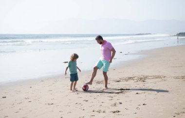 Mutlu baba-oğul futbol oynuyor. Yaz tatilinde eğleniyorlar. Kumsalda aile tatili, çocukluk.