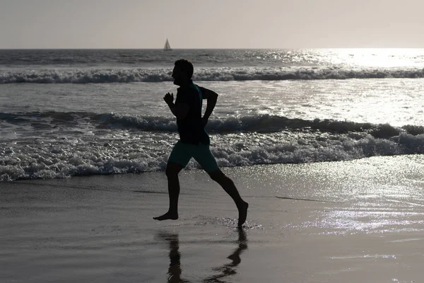 Hombre atlético corredor silueta correr en la playa de verano con agua de mar y sol, motivación — Foto de Stock