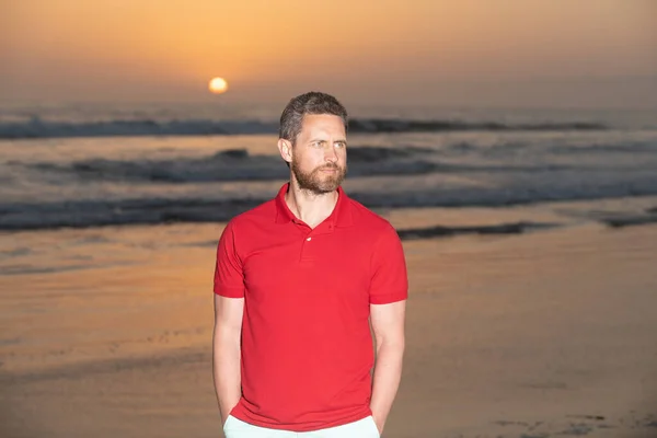 Homem bonito barbudo na camisa de verão na praia com pôr do sol sobre o mar, vista romântica — Fotografia de Stock