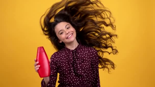 Felice bella bambina agitando i suoi lunghi capelli ricci presentando shampoo, bellezza — Video Stock