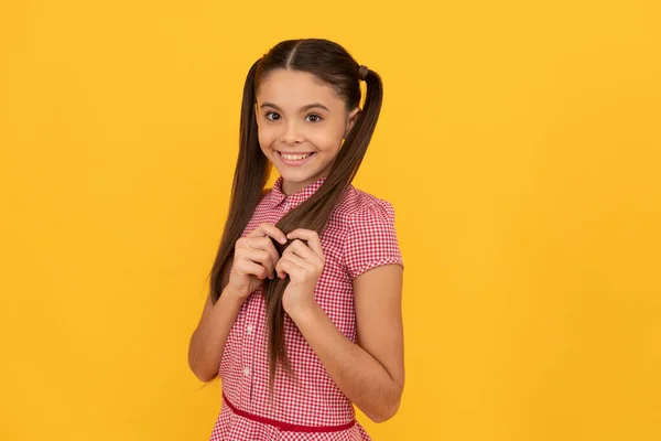 Belle fille enfant avec timide sourire toucher cheveux fond jaune, timide — Photo