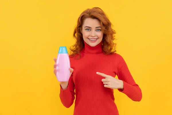 Ragazza capelli ricci puntando il dito sulla bottiglia di shampoo. pubblicità condizionatore per capelli. — Foto Stock