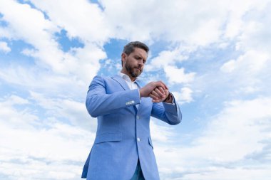 Takım elbiseli yakışıklı, olgun iş adamı. Kol saatini kontrol et. Gökyüzü arka planında, dakiklik..