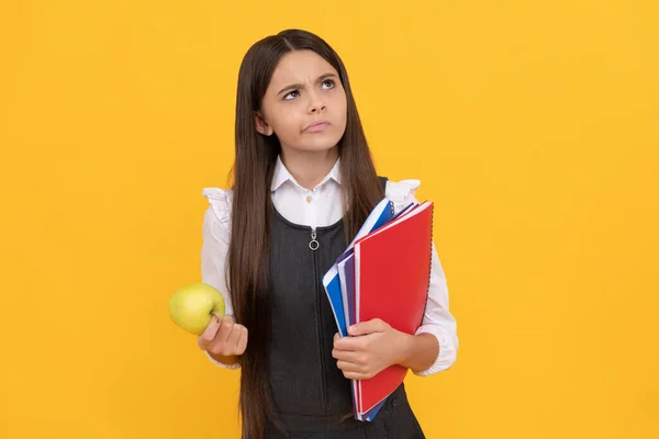Grave criança em idade escolar pensar segurando maçã e livros fundo amarelo, pensando — Fotografia de Stock