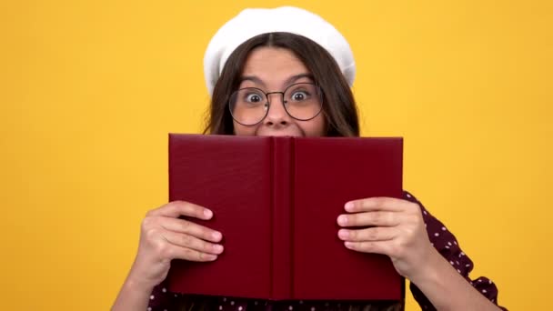 Szczęśliwy zaskoczony nerd nastolatek dziewczyna w okularach ukrywa się za czytanie książki podejmowania inteligentny twarz, czytelnik — Wideo stockowe
