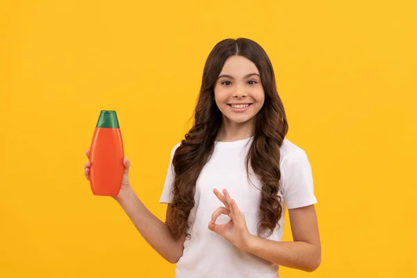 Χαρούμενο παιδί με μακριά μαλλιά προσφορά σαμπουάν μπουκάλι δείχνουν ok χειρονομία, πρόταση προϊόντος — Φωτογραφία Αρχείου