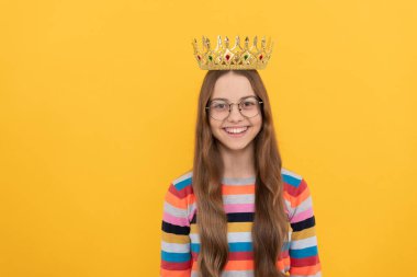 Gözlüklü mutlu çocuk sarı arka planda kraliçe tacı takıyor, zafer