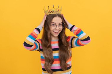 happy teen girl in glasses wear princess crown on yellow background, prom