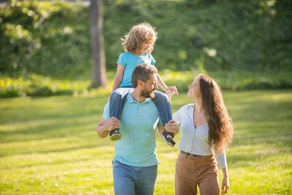 Anne ve babanın mutlu bir ailesi var. Çocuğunu omuzlarında taşıyorlar. Yazın açık havada, koruyucu ailede.