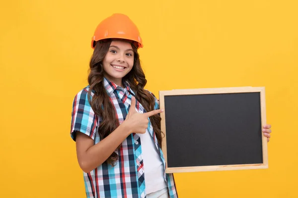 Gülümseyen genç işçi kız kara tahtayı işaret ediyor. Çocuk reklamları günü. — Stok fotoğraf