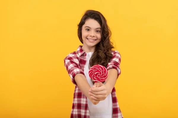 Gelukkig kind met lang krullend haar show lolly karamel snoep op gele achtergrond, tandheelkundige verzorging. — Stockfoto