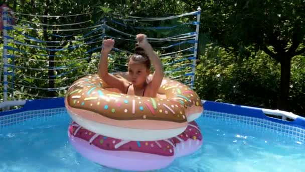 Ragazza felice bambino divertirsi galleggiante in piscina ciambella galleggia nella soleggiata giornata estiva, galleggiante — Video Stock