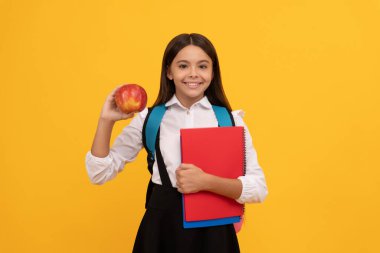 Happy kid go back to school holding apple and books yellow background, knowledge day