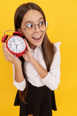 surprised nerd child listen the alarm clock ringing. school kid in uniform and glasses showing time.