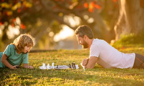 Happy family of dad and son boy playing chess on green grass in park outdoor, concentration — Photo