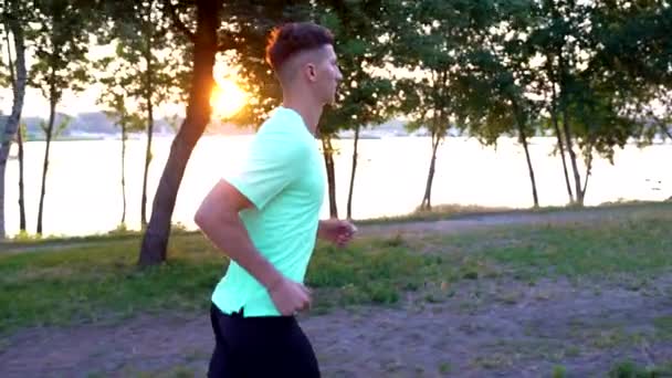 Healthy guy in sportswear running at river outdoor, sport training slow motion — Video
