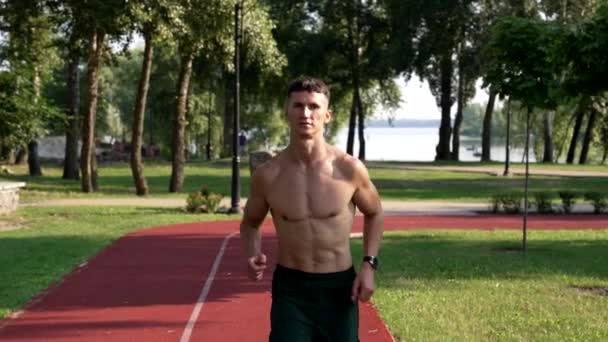 Sportive guy with muscular body runs on running track in park, sporty — Stock Video