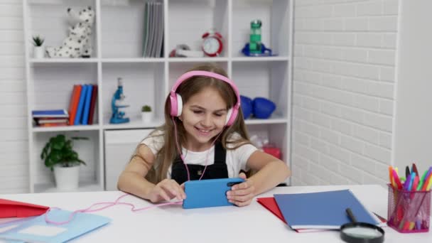 Happy teen girl listen music in headphones watching video on smartphone in classroom, home schooling — Vídeo de stock