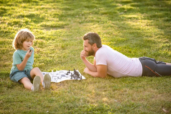 Père et fils jouant aux échecs sur l'herbe dans le parc. la fête des pères. famille heureuse. parentalité et enfance. — Photo