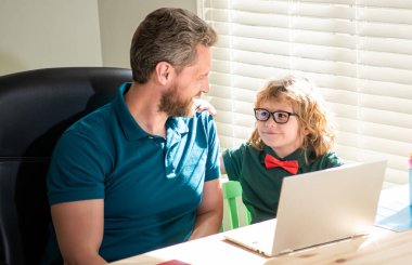 Mutlu bir baba oğlunun evde dizüstü bilgisayarla çalışmasına yardım ediyor, eğitim görüyor.