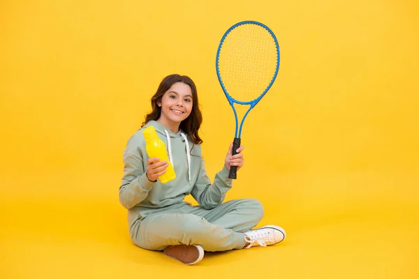 Glad barn hålla badminton racket och dricka vatten från flaska på gul bakgrund, hälsa. — Stockfoto