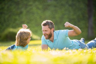 Ebeveyn, küçük çocuk çimlerin üstündeyken rahatlar. Mutlu baba ve çocuklu yaz günü.