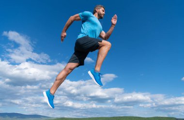 Spor kıyafetleri içinde koşan kaslı bir adam gökyüzü arka planında meydan okuyor.