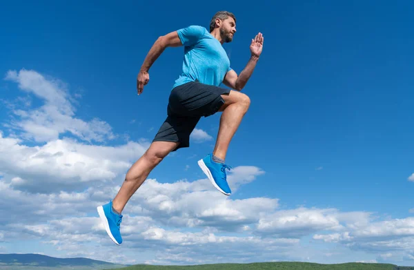 Spor kıyafetleri içinde koşan kaslı bir adam gökyüzü arka planında meydan okuyor.