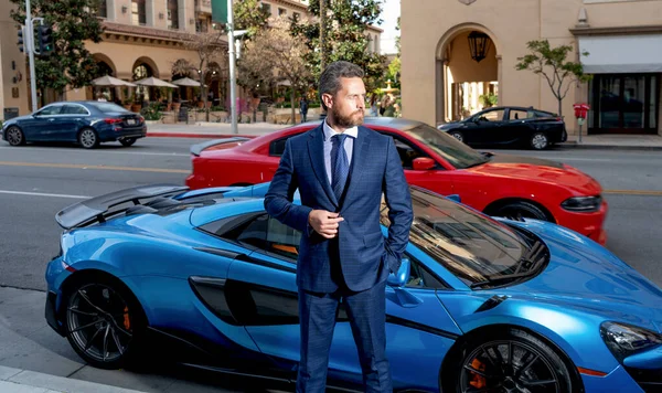 Resmi takım elbiseli yakışıklı bir emlakçı lüks otomobilin yanında duruyor, araba sigortası var.