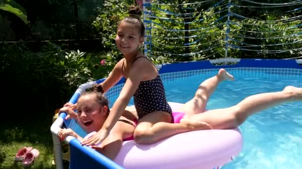 Happy children splash down from swimming ring in outdoor swimming pool, fun — стоковое видео