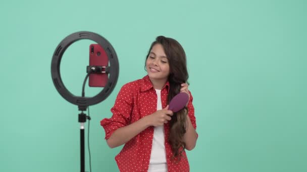 Χαμογελαστό παιδί blogger ομορφιά προώθηση βούρτσα μαλλιών και χτένισμα μακριά κυματιστά μαλλιά της, προώθηση — Αρχείο Βίντεο