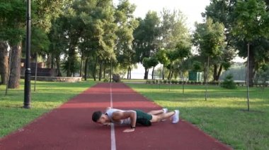 Genç sporcu, parkta burpee egzersizi yapıyor.