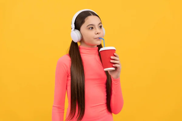 Grave enfant écouter de la musique dans les écouteurs boire de tasse en papier sur fond jaune, café — Photo