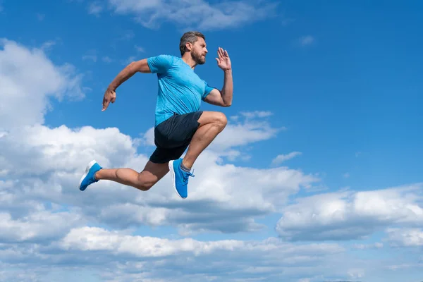 Енергійний спортсмен з м'язистим тілом біжить у спортивному одязі на фоні неба, витривалість — стокове фото
