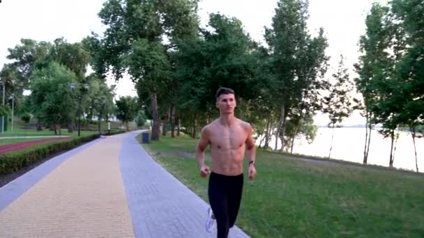 Uomo sportivo con corpo muscoloso che corre al fiume all'aperto, corsa mattutina — Video Stock