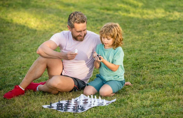 Tutoría. papá y el niño juegan juego de lógica. padre e hijo jugando ajedrez en la hierba en el parque. — Foto de Stock