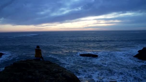 Mujer solitaria en chaqueta sentada en el mar ondulado con cielo dramático, soledad — Vídeo de stock